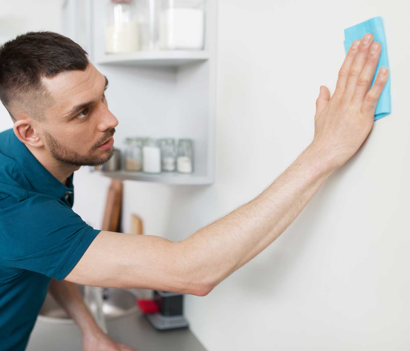 man cleaning kitchen wall to prepare for hanging wallpaper