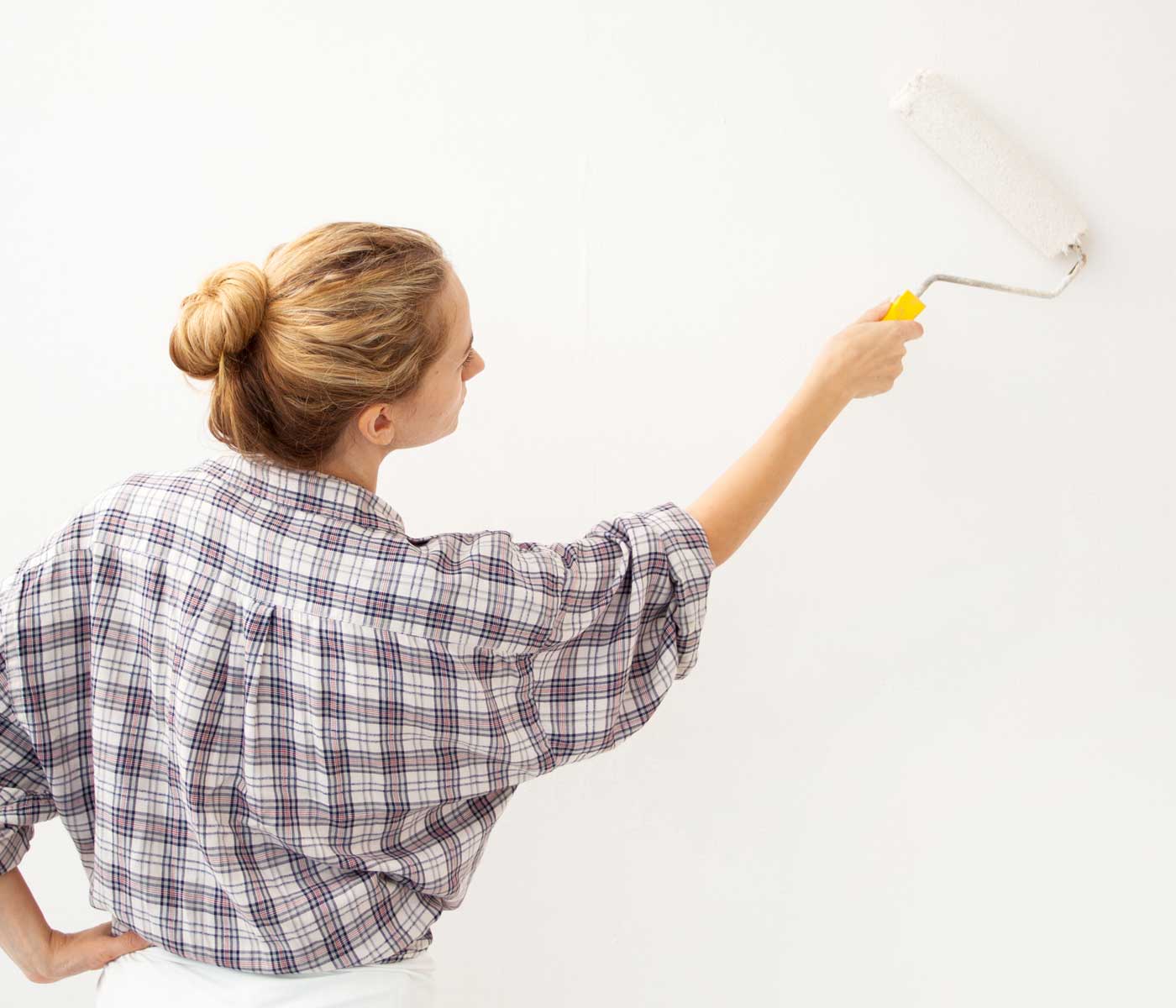 woman applying a coat of acrylic primer to a wall to prepare for installing wallpaper