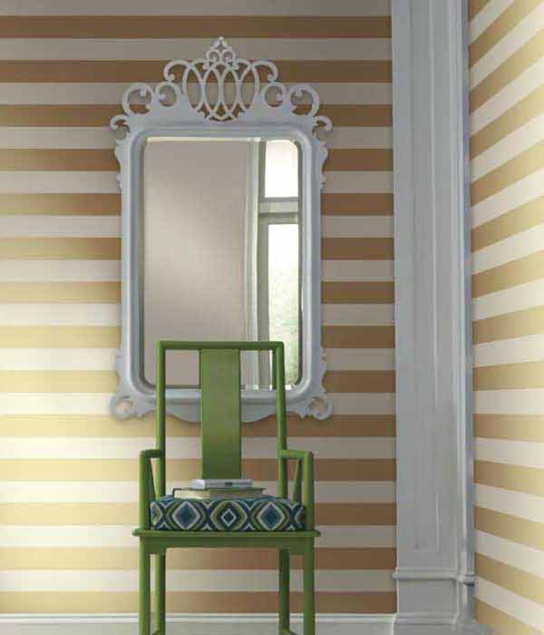 chair and mirror in a corner of a room with wallpaper that features horizontal lines