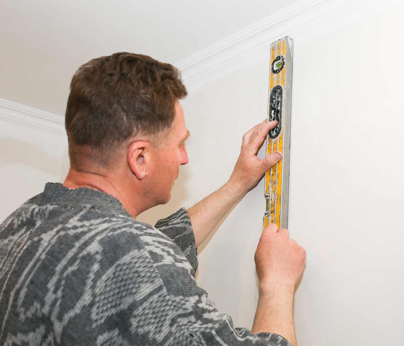 man making a level vertical line on a wall to prepare for hanging wallpaper straight